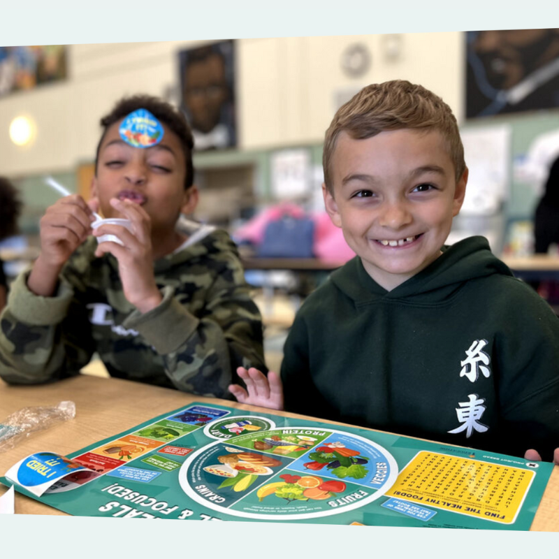 Two young boys grin at the cafeteria lunch table