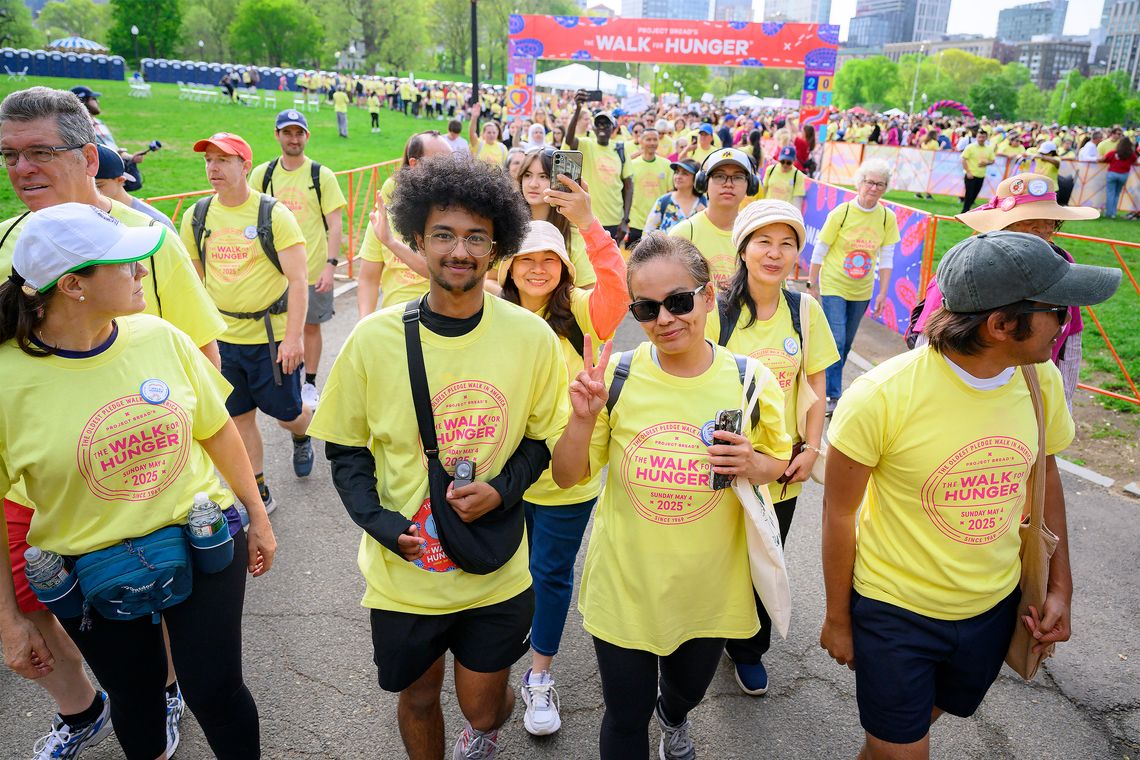 A crowd of walkers in bright yellow shirts walk along the Common under The Walk for Hunger starting line