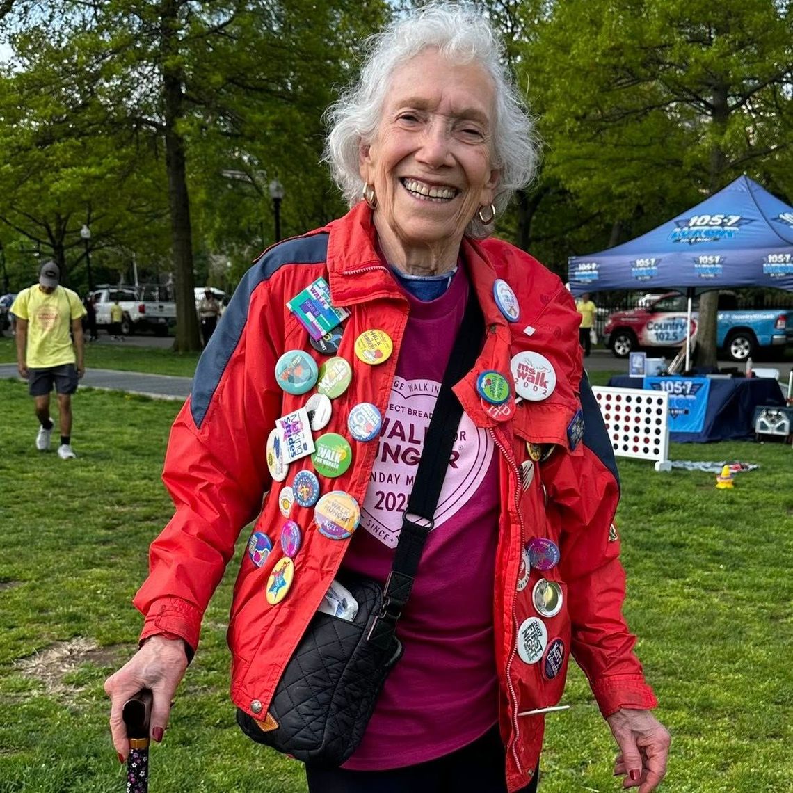 Older women holds a cane, wearing her Heart and Sole shirt, decked out in buttons from over the years