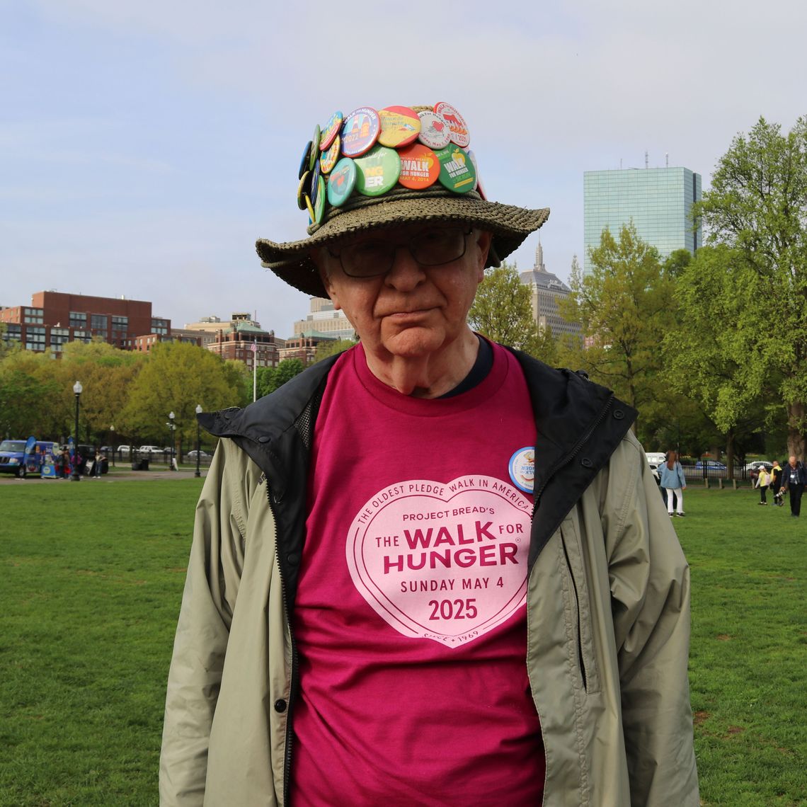 An older man wears a hat decked with Walk for Hunger buttons.
