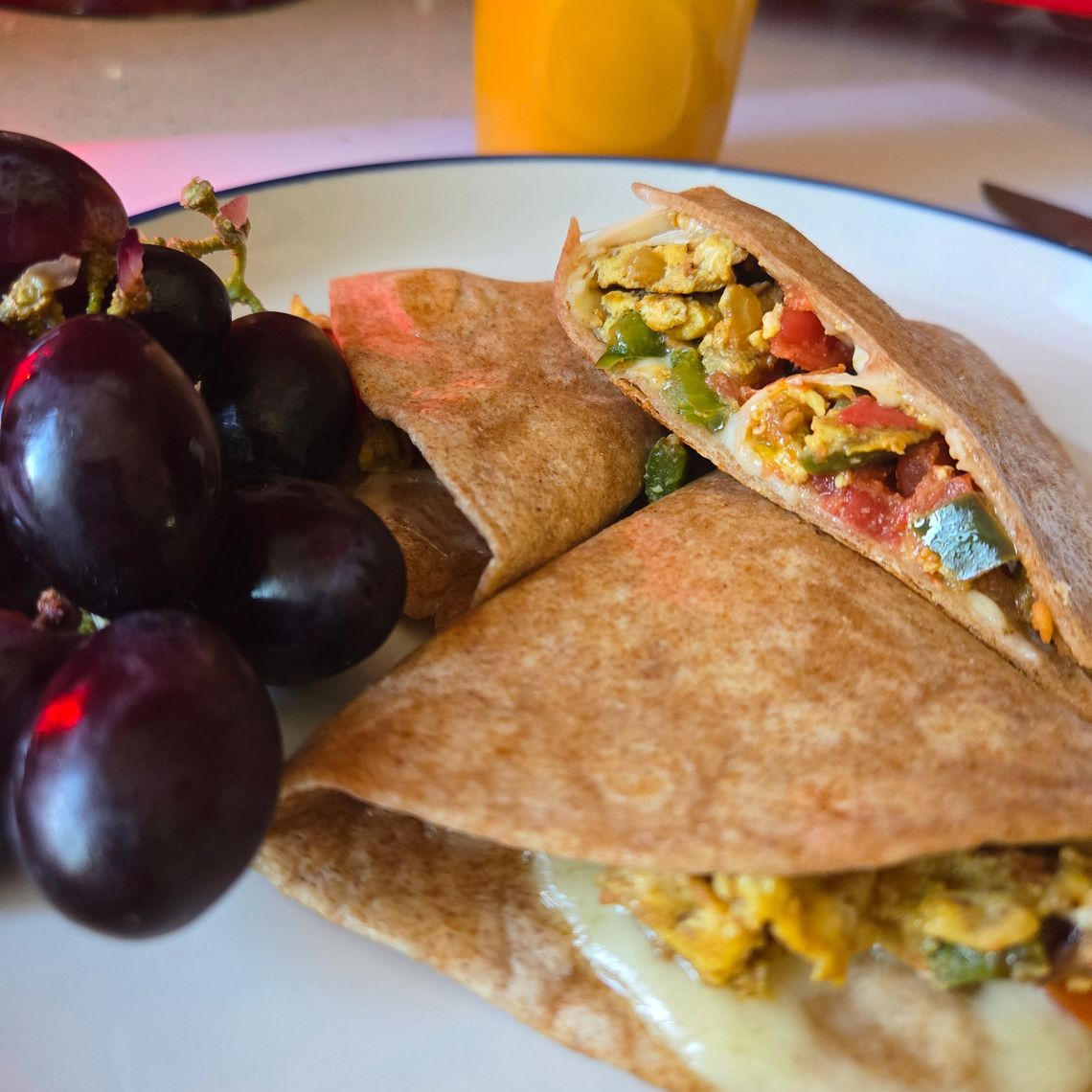 A breakfast quesadilla plated with grapes and a glass of orange juice