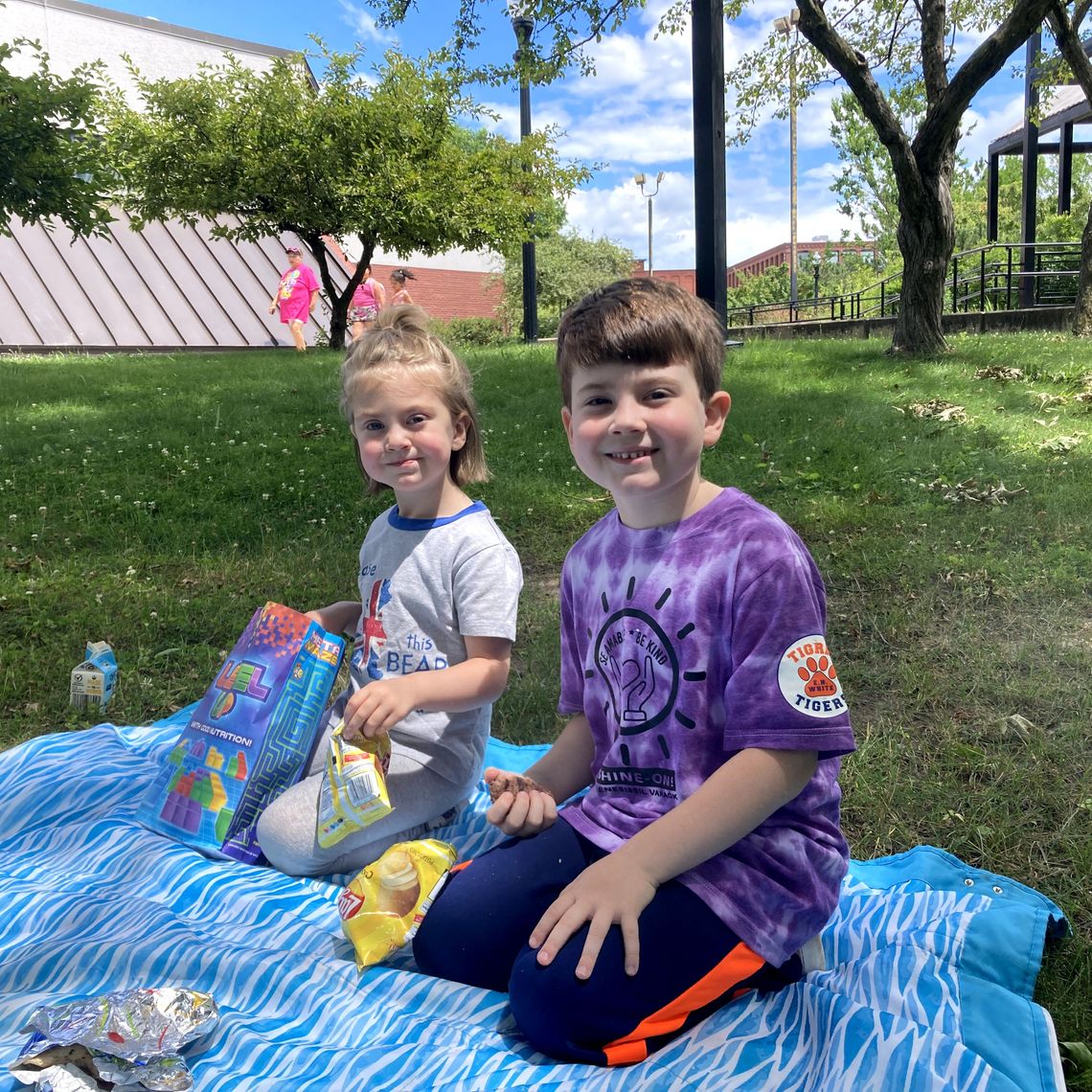 two kids on a blanket eating a meal outside