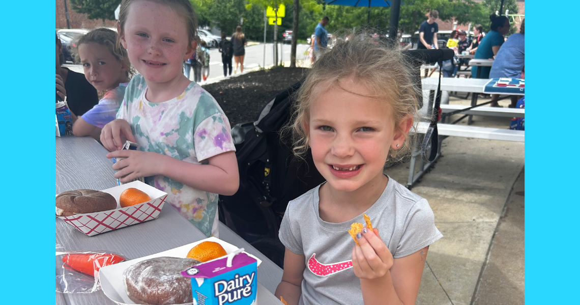 two girls smiling and eating at a picnic table