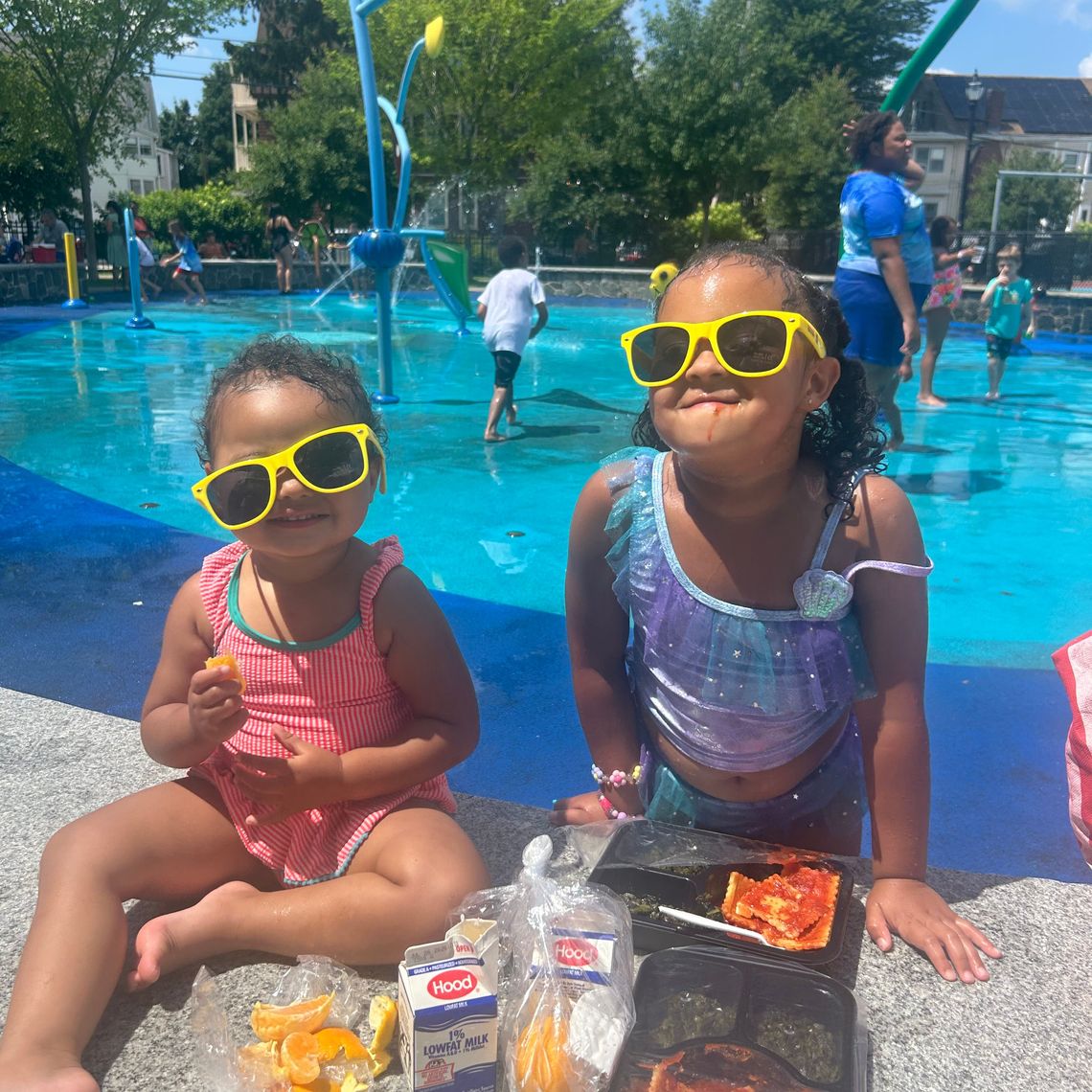 2 sisters smiling in sunglasses eating lunch by the pool