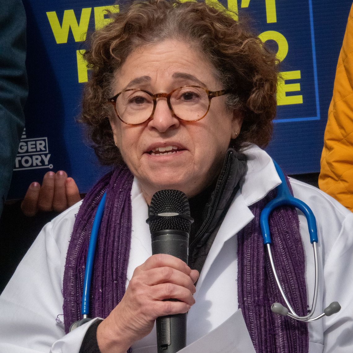Dr. Diana Cutts, MD, wearing her stethoscope and white lab coat, speaks passionately into the microphone at Rally for SNAP on MA State House steps.